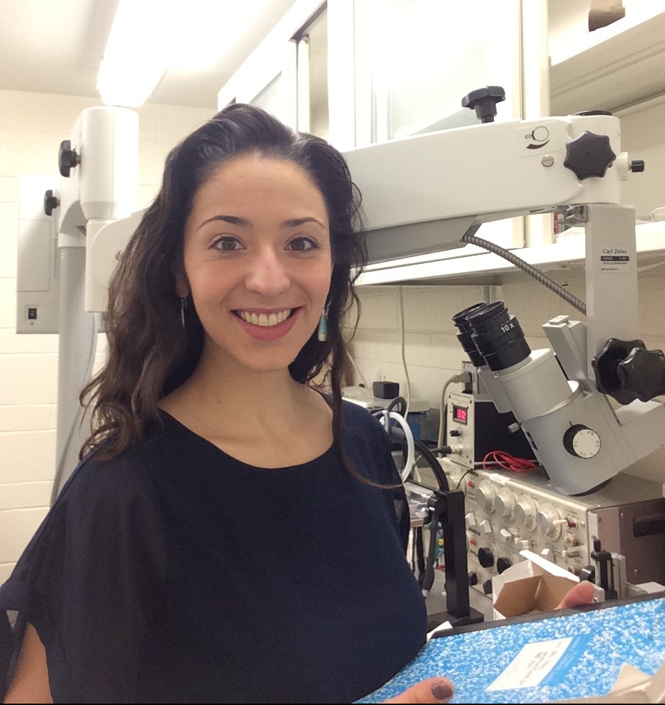 Photo of Amy Strauss in a lab, smiling and holding a lab notebook.